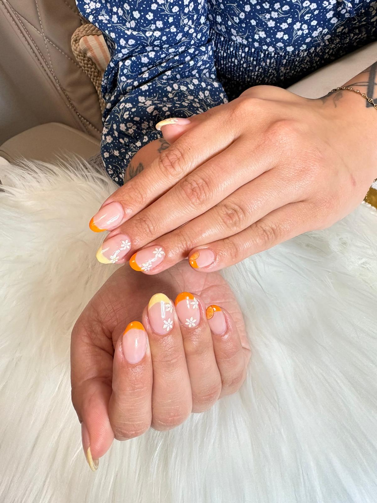 Manucure aux pointes orange et jaune, décorée de petites fleurs blanches