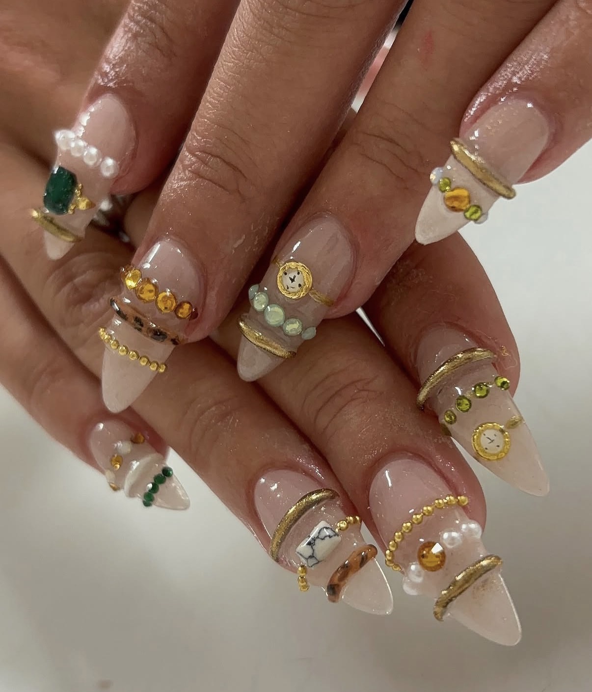 Ongles nude ornés de perles, bijoux et lignes dorées